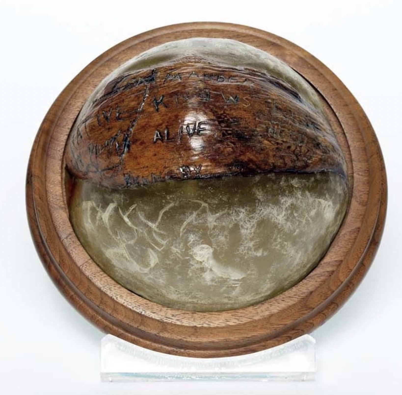 Coconut shell with message from Lieutenant John F. Kennedy carved on the surface. The shell is encased in plastic and mounted on wood to create a desk paperweight.